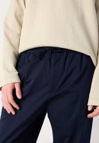 Beige teksturert langermet topp parret med marineblå joggebukser. Bukser med lommer på sidene og en glatt overflate. Ingen synlige mønstre eller detaljer.