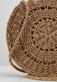 Sac à main rond en paille tissée avec motif en spirale et design en tissage ouvert, avec une sangle tressée assortie sur un fond uni.