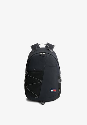 Sac à dos noir Tommy Jeans avec bretelles rembourrées, poche avant en mesh avec cordon élastique et compartiment principal zippé sur fond blanc.
