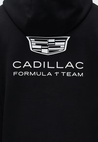 Svart hoodie bak med vit Cadillac-logotyp ovanför texten "CADILLAC FORMULA 1 TEAM" i versaler.