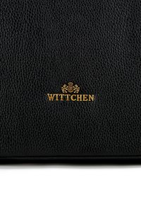 Zwarte leren tas met een goudkleurig "Wittchen" logo. Heeft een geprofileerde afwerking en een eenvoudig, elegant ontwerp.