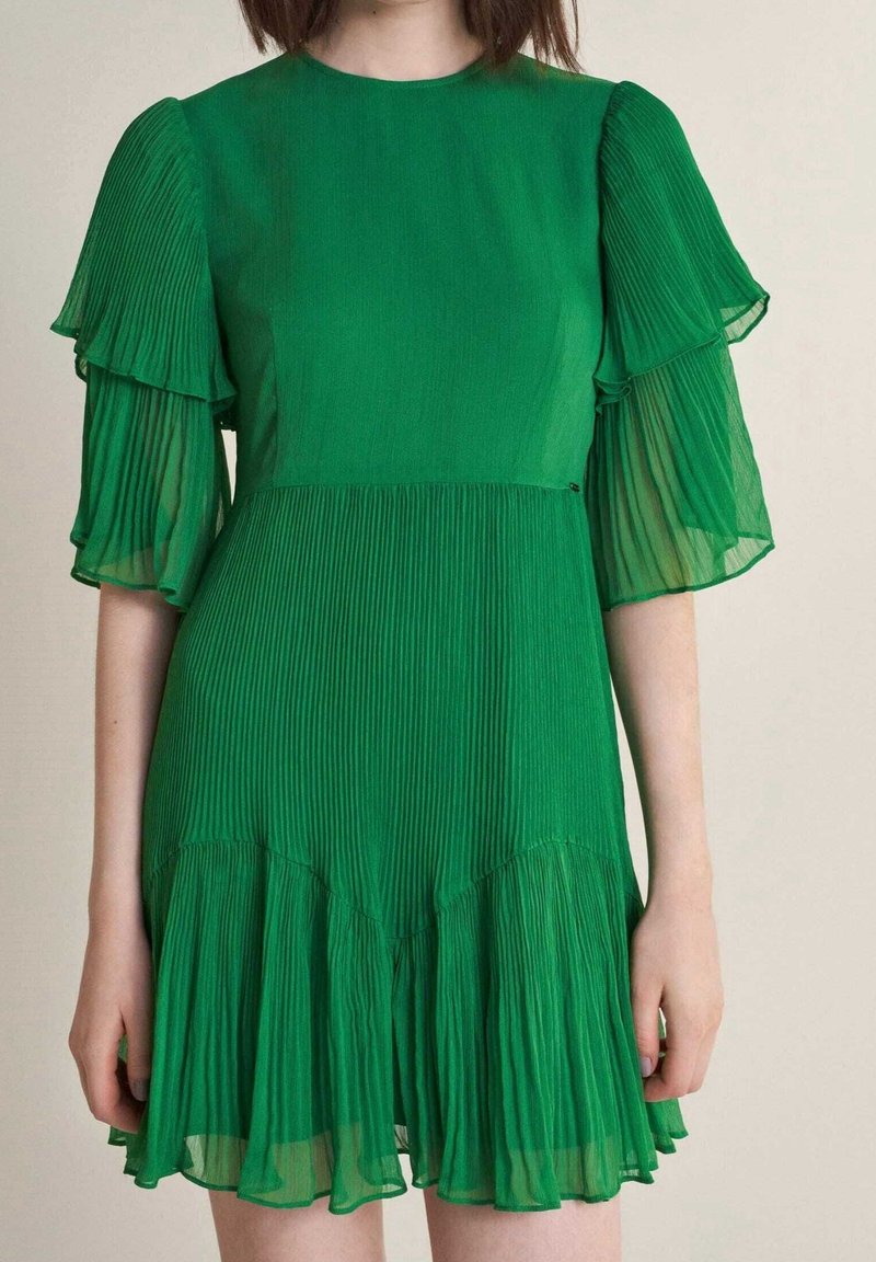 Robe plissée verte avec des manches courtes évasées en tissu transparent. Design fluide en forme de A avec un ourlet à volants superposés et une texture douce.