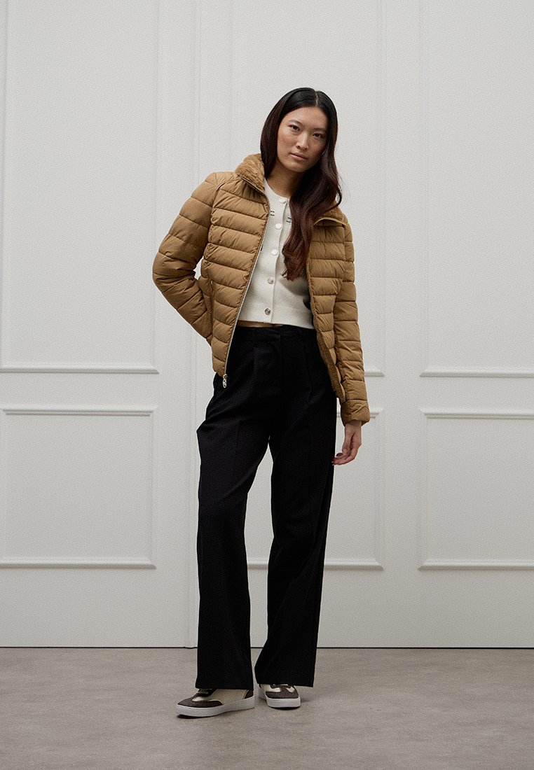 Braune gesteppte Daunenjacke, cremefarbenes Strickoberteil und schwarze, weit geschnittene Hosen. Das Outfit verfügt über einen Reißverschluss und Druckknopfdetails.