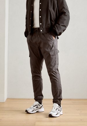 Graue Cargo-Hosen mit elastischen Bündchen, seitlichen Taschen und einem Kordelzugbund, kombiniert mit weißen und grauen Sport Sneakers.