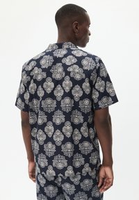 Camicia a maniche corte in tessuto blu navy con intricati motivi floreali e paisley bianchi. Fit casual con colletto e dettagli cuciti sulla schiena.