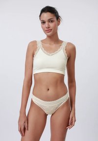 Cream-colored bralette with lace trim, ribbed texture, and matching lace briefs. Each has scalloped edges and a fitted design.
