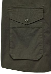 Olijfgroene stof met een gestructureerde afwerking, voorzien van een grote klepzak die wordt beveiligd door een knop en contrasterende stikdetails.