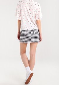 Vit blus med röd läpptryck, korta volangärmar; svartvitrutig minikjol med slitna kanter och bakfickor. Vita sneakers.