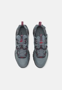 Grå sportskor med ovandel i mesh, texturerade detaljer, röda accenter, tjock gummisula och framträdande snören. Har en dragflik på hälen.