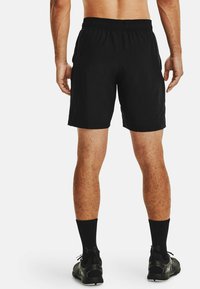 Svarta sportshorts med resårmidja, slät textur och längd till mitten av låret. Bärs med svarta strumpor och sneakers.