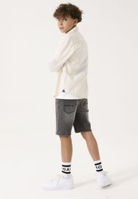 Camisa de manga larga beige claro, pantalones cortos de mezclilla grises, zapatillas blancas y calcetines a rayas en blanco y negro. Diseño simple con un ajuste casual.