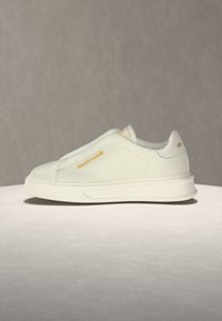 Sneaker blanc slip-on avec semelle épaisse et logo doré "roberto cavalli" sur le côté et à l’arrière, présenté sur une surface claire avec un fond uni.