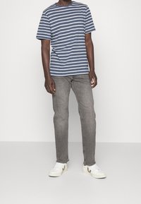 Pruhované modro-bílé tričko s krátkým rukávem v kombinaci s šedými slim-fit džíny a bílými teniskami s béžovými detaily. Jednoduchý, neformální outfit.