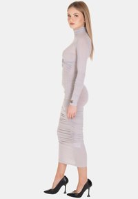 Abito lavanda aderente a maniche lunghe con texture arricciata, collo alto e lunghezza a metà polpaccio, abbinato a tacchi alti neri.