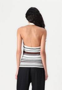 Ribbed crop top in white with multicolored horizontal stripes. Features a halter neckline and open back design. Smooth texture.