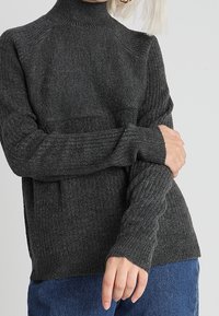 Ciemnoszary sweter dziany z wysokim kołnierzem, z żebrowanymi rękawami i luźnym krojem, wykonany z teksturowanej przędzy.