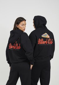 Μαύρες φούτερ με κουκούλα διαθέτουν το κείμενο "Billiards Club" σε κόκκινο χρώμα στο πίσω μέρος, συνοδευόμενο από ένα πολύχρωμο γραφικό με μπαλάκια του μπιλιάρδου.