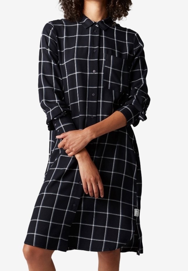 Svart och vit rutig skjortklänning med krage, långa ärmar, en bröstficka och knäppning, tillverkad av ett lätt tyg.