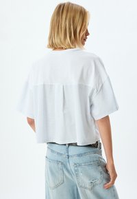 Gemütliches T-Shirt mit einem oberen Teil aus weißem Chambray und einem unteren Abschnitt in leicht blauen Streifen, ausgestattet mit kurzen Ärmeln und einem lässigen Schnitt.