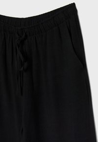 Zwarte broek met een elastische tailleband, een trekkoord en zijzakken. De stof lijkt zacht en licht gestructureerd, geschikt voor casual dragen.