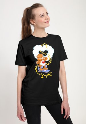 Sort t-shirt med et tegneserie bjørn på en skateboard, omgivet af skyer og stjerner i gul og hvid, med et hjerte-design på bjørns t-shirt.
