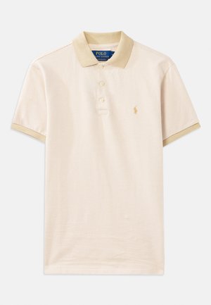 Polo beige avec un motif texturé, col marron clair contrastant, patte de boutonnage à trois boutons et un petit logo en or brodé sur la poitrine.