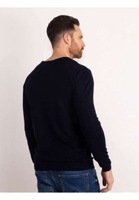 Maglione lungo a maniche con scollo a girocollo in blu navy, con polsini e orlo a costine. Realizzato in tessuto morbido, presenta una texture liscia.