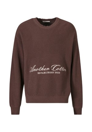 Brun ribbet striktrøje med rund halsudskæring. Har hvid tekst "Another Cotton Established 2023" på forsiden og ribbede manchetter.