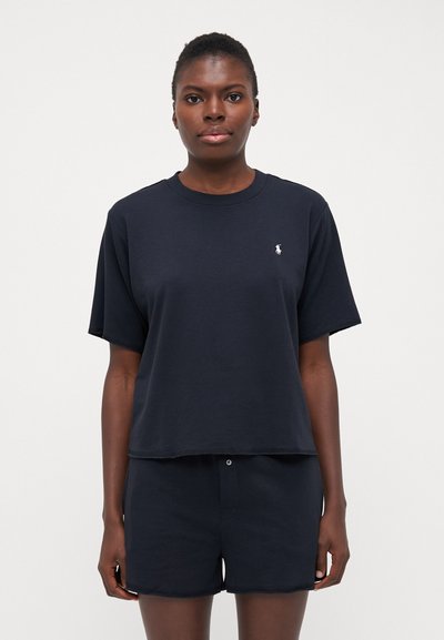 Tricou din bumbac, de culoare albastru marin, cu mâneci scurte și guler rotund, având un logo alb pe piept, purtat împreună cu pantaloni scurți asortați, de aceeași nuanță.