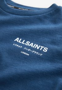 Niebieska bawełniana bluza z białym napisem „ALLSAINTS” oraz dodatkowymi znakami, widocznym przeszyciem i okrągłym dekoltem.