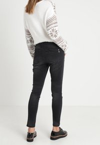 Černé úzké džíny z denimu s středním pasem, s decentními zadními kapsami a opotřebenými detaily, spárované s pohodlným bílým svetrem.