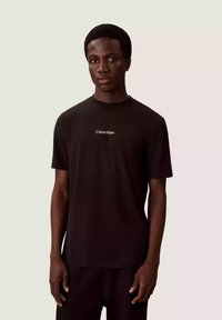 Czarny bawełniany t-shirt z okrągłym dekoltem i krótkimi rękawami, z białym haftowanym logo "Calvin Klein" na piersi.