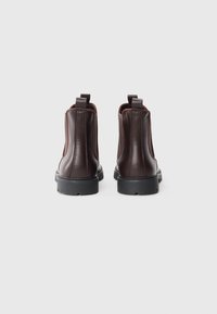 Botas Chelsea de cuero marrón con acabado texturizado, paneles laterales elásticos y tiradores. Suelas de rubber negro para mayor durabilidad.