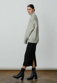 Lys grå, højhalset sweater parret med en sort, knælang nederdel med en sideslids. Modellen har sorte, hælede ankelstøvler på.