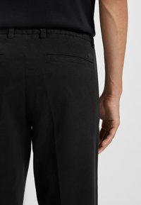 Czarne spodnie wykonane z miękkiego materiału, o dopasowanym kroju, z dwiema tylnymi kieszeniami oraz dyskretną metką marki na pasku.