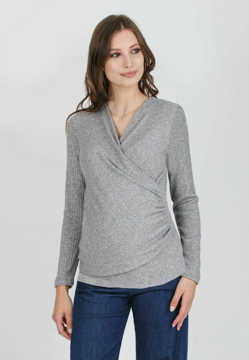 Grau gerippter langärmeliger Oberteil mit Wickeldesign, featuring einem tiefen V-Ausschnitt und gerafftem Seitendetail, kombiniert mit blauen Jeans.