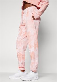 Lettvekt, tie-dye joggebukser i myk rosa med avslappet passform, elastisk midje, sidelommer og smale mansjetter, kombinert med hvite joggesko.