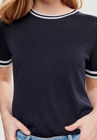 Námornícké triko s krátkým rukávem a kulatým výstřihem, zdobené bílými pruhovanými akcenty na límci a rukávech, vyrobené z měkké, texturované látky.