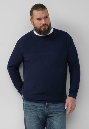 Marineblauwe trui met lange mouwen en een licht gestructureerd oppervlak, met geribde manchetten en tailleband, gedragen over een wit shirt. Casual pasvorm.