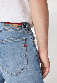 Lys blå denimjeans med rett snitt. Har en rød brodert logo på baklomma og en flerfarget merkeetikett på linning.