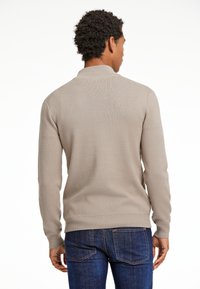 Beige neule, jossa on teksturoitu neulekuvio, ribbineuleiset hihansuut ja helma, sekä klassinen kaulus. Yhdistetty tummansinisiin farkkuihin.