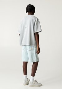 Maglietta grigia over-size con dettaglio grafico sul retro, abbinata a pantaloni corti in denim blu chiaro e scarpe da ginnastica beige, completata da calze bianche a crew.