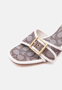 Chaussure pour femme à bout pointu en tissu marron à motifs, avec une bordure blanche et une sangle à boucle carrée dorée sur le devant.