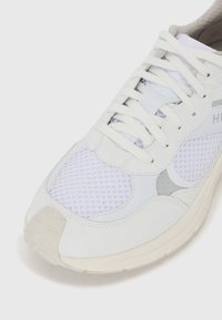 White athletic shoe with mesh and leather panels, laces in the center, rounded toe, and subtle gray accents on the sides and heel.