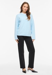 Svetlo modra, priložnostna majica z dolgimi rokavi in okroglim izrezom, kombinirana s črnimi hlačami. Ozek kroj, mehka tekstura in preprost dizajn.