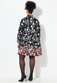 Abito nero con motivo floreale bianco e orlo floreale multicolore. Maniche lunghe, gonna svasata, abbinato a scarpe nere con tacco alto.