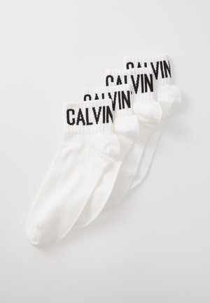 Calcetines de algodón blancos tipo crew con el logo negro "CALVIN" en los puños acanalados, que presentan una textura suave y un diseño atlético clásico. Paquete de cuatro pares.