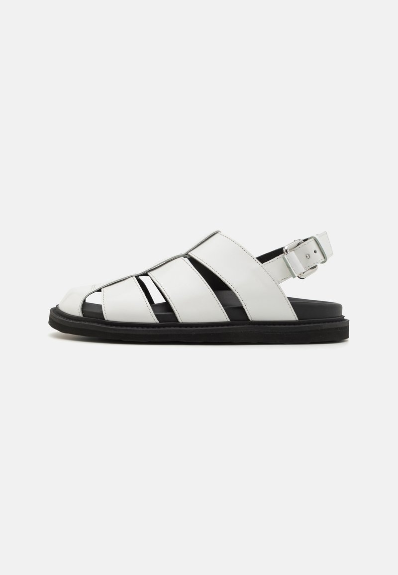 Sandal in pelle bianca con punta aperta, dotata di fessure e di un cinturino alla caviglia posteriore. Suola in gomma nera per una buona aderenza. Design minimalista.