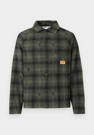 Koszula w oliwkowo-zieloną i czarną kratę z długim rękawem, brązowymi guzikami, kołnierzykiem oraz małą beżową naszywką na kieszeni na piersi.