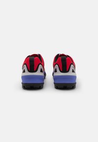 Rote und schwarze Sportschuhe mit einer gepolsterten lila Sohle, ausgestattet mit einer strukturierten Gummisohle und einem Zugband an der Rückseite für einfaches Anziehen.